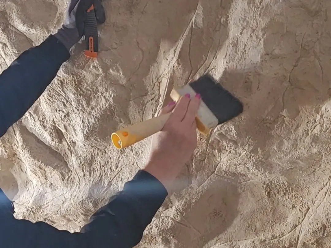 Hands shaping and finishing the surface of a sculpted rock wall by hand