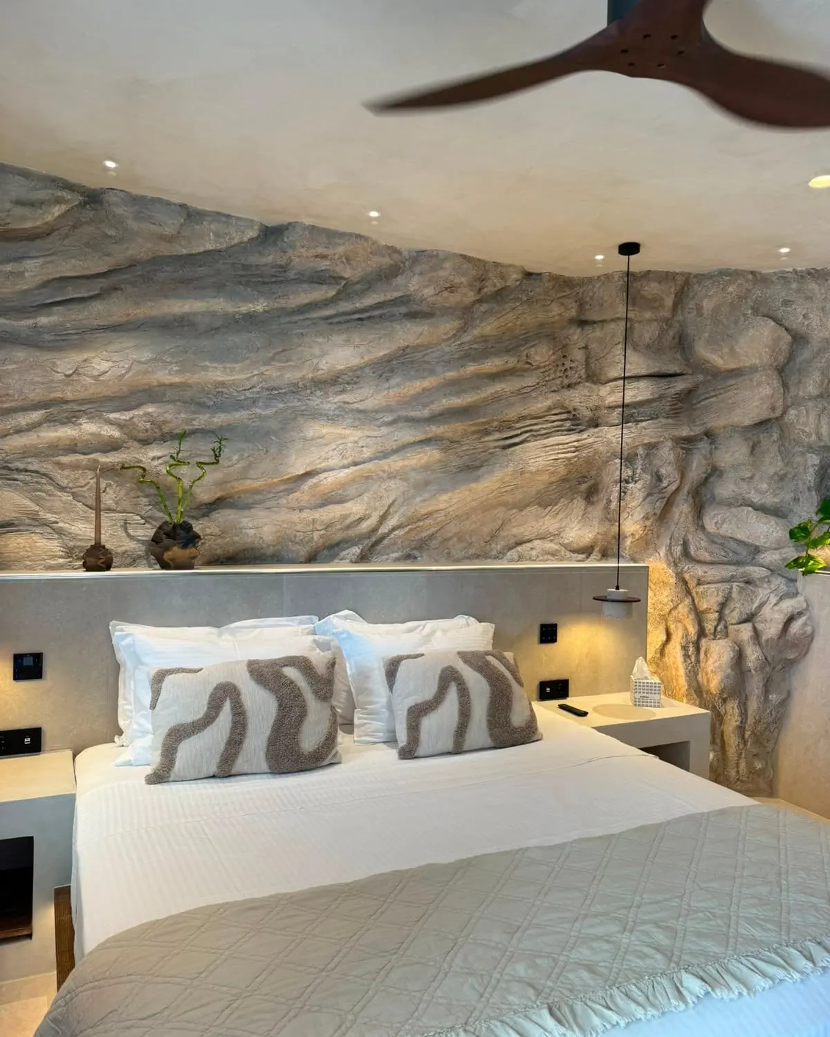 The bed set beneath the sculpted wall, with pendant lights hanging either side