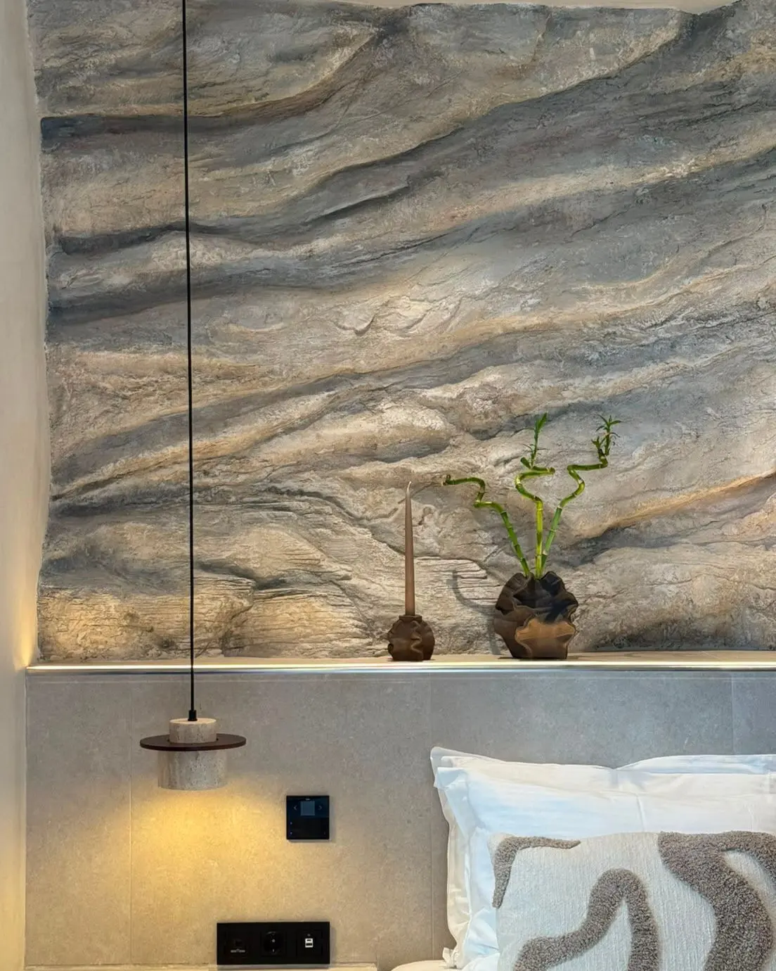 A detail of the layered rock surface above the headboard, with a plant on the lit shelf below it