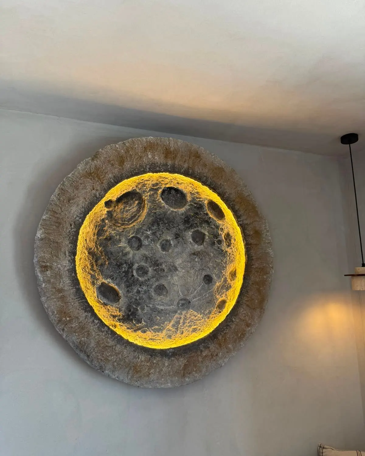 A circular moon relief mounted on the wall, its cratered surface lit gold from behind