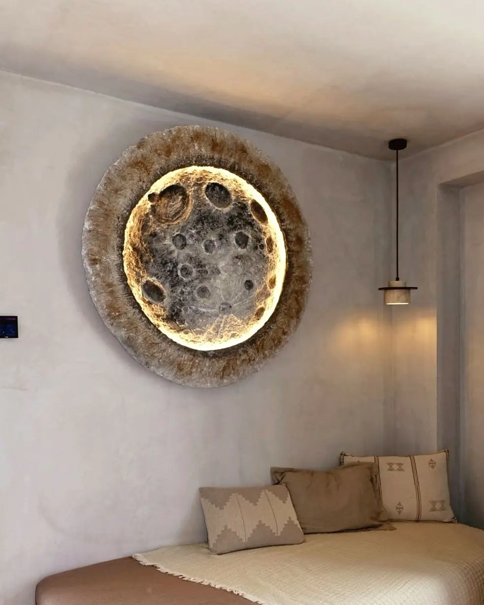 The same moon relief above a low daybed, lit white against a pale plaster wall