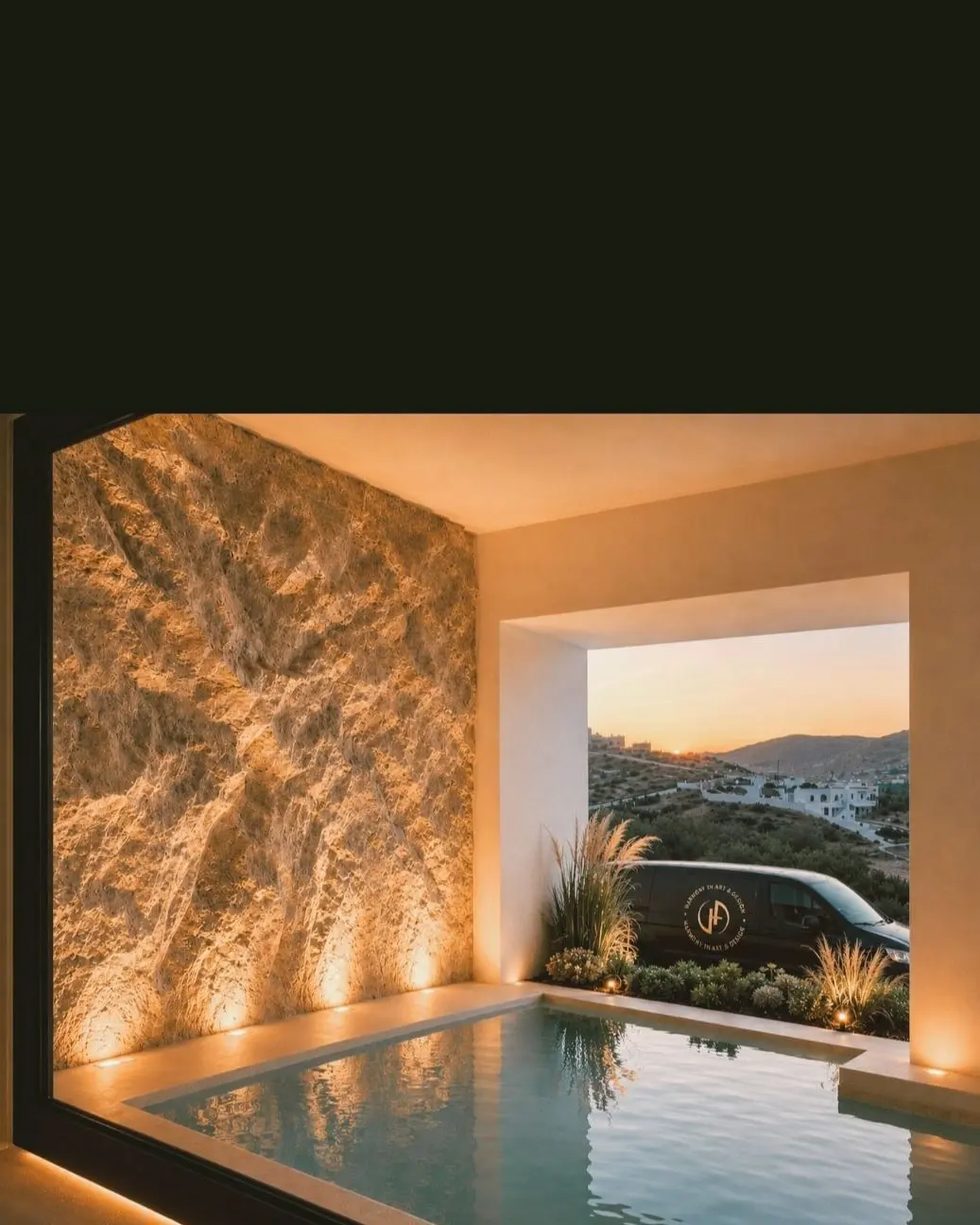 A sculpted rock wall lit from the floor beside a pool at dusk