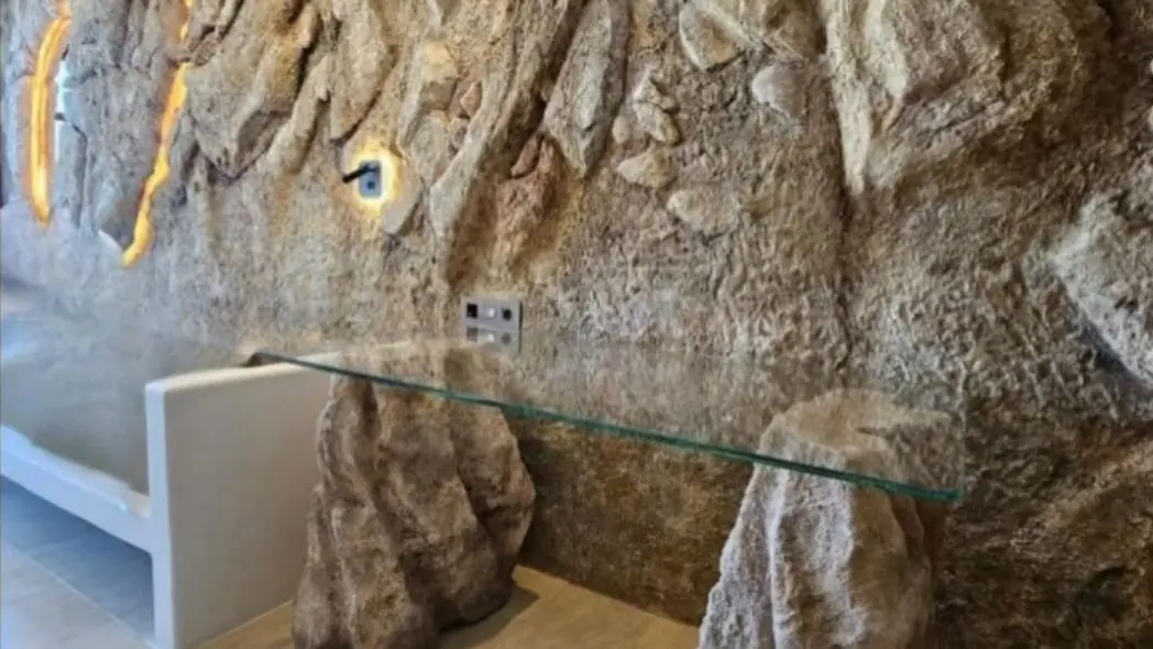 A cave-like room with sculpted rock walls lit from within, and a glass table resting on carved stone legs