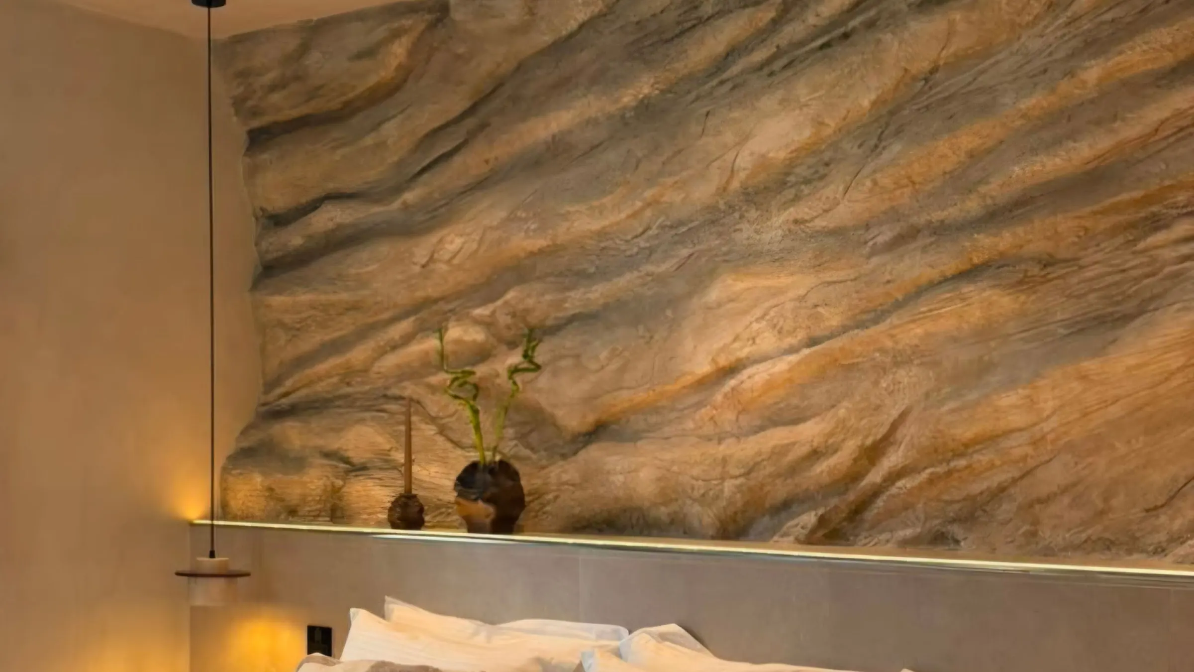 A sculpted rock wall running the width of a finished suite, lit from a recessed channel above the bed