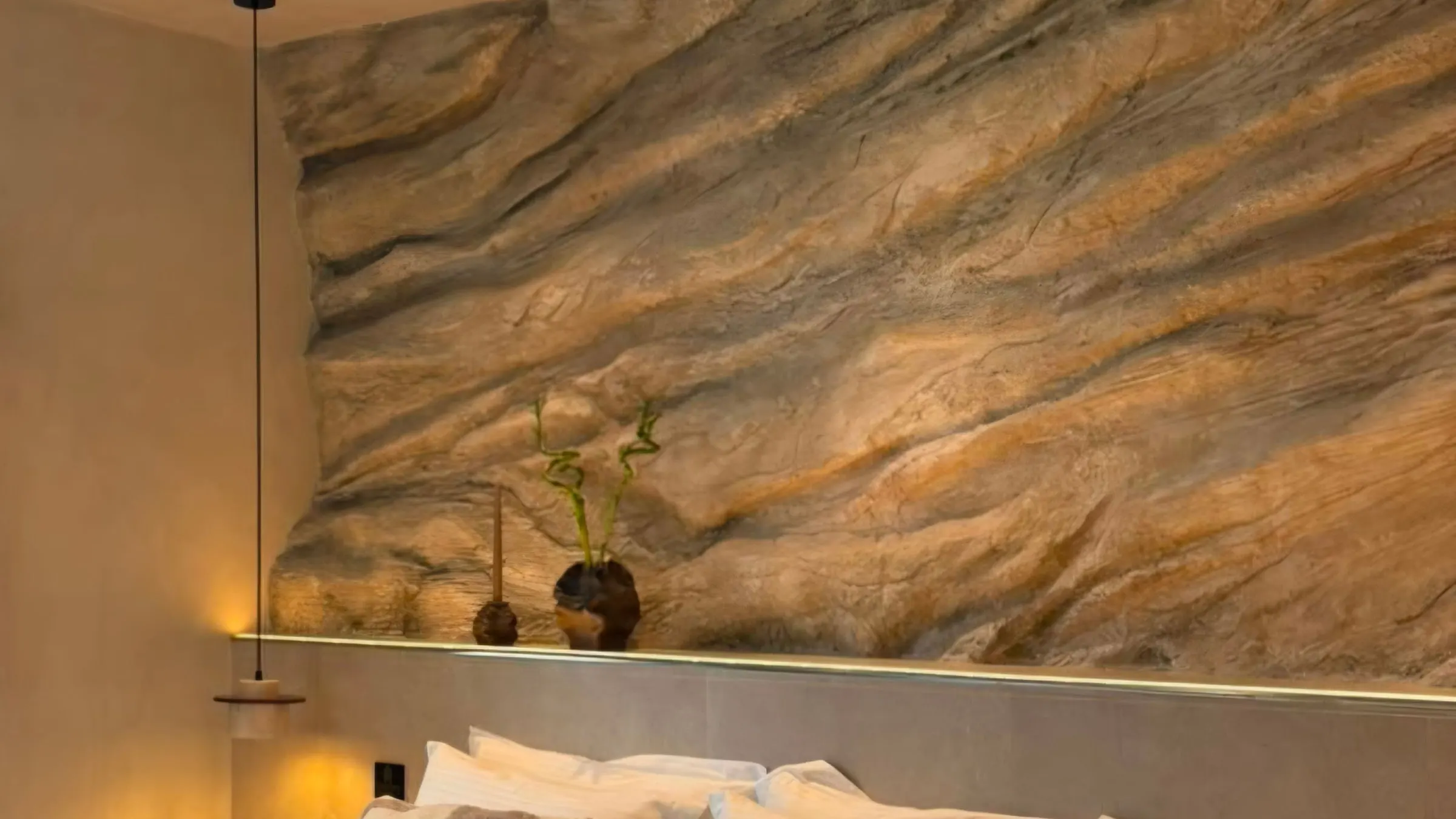 A sculpted rock wall running the width of a finished suite, lit from a recessed channel above the bed