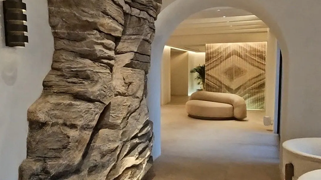 A hand-sculpted rock archway opening into a bedroom, lit from below along the floor